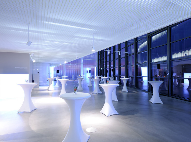 Modern gestalteter Eventbereich mit weiß eingedeckten Stehtischen, stimmungsvoller blauer Beleuchtung und großer Fensterfront bei Nacht.