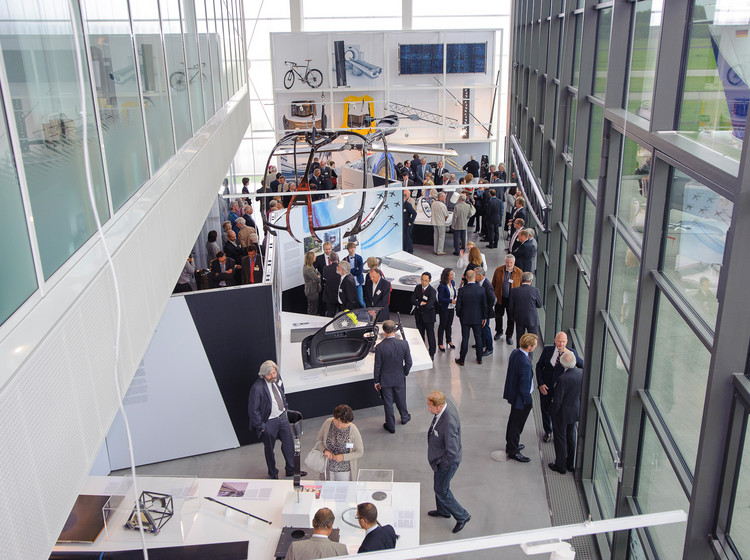 Blick von oben auf eine Messe oder Ausstellung mit mehreren Ständen und Besuchern in heller, verglaster Halle mit modernem Design.